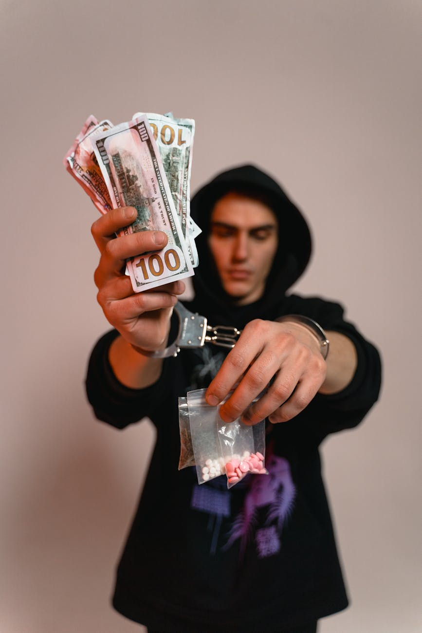a man in handcuffs holding cash and illegal drugs